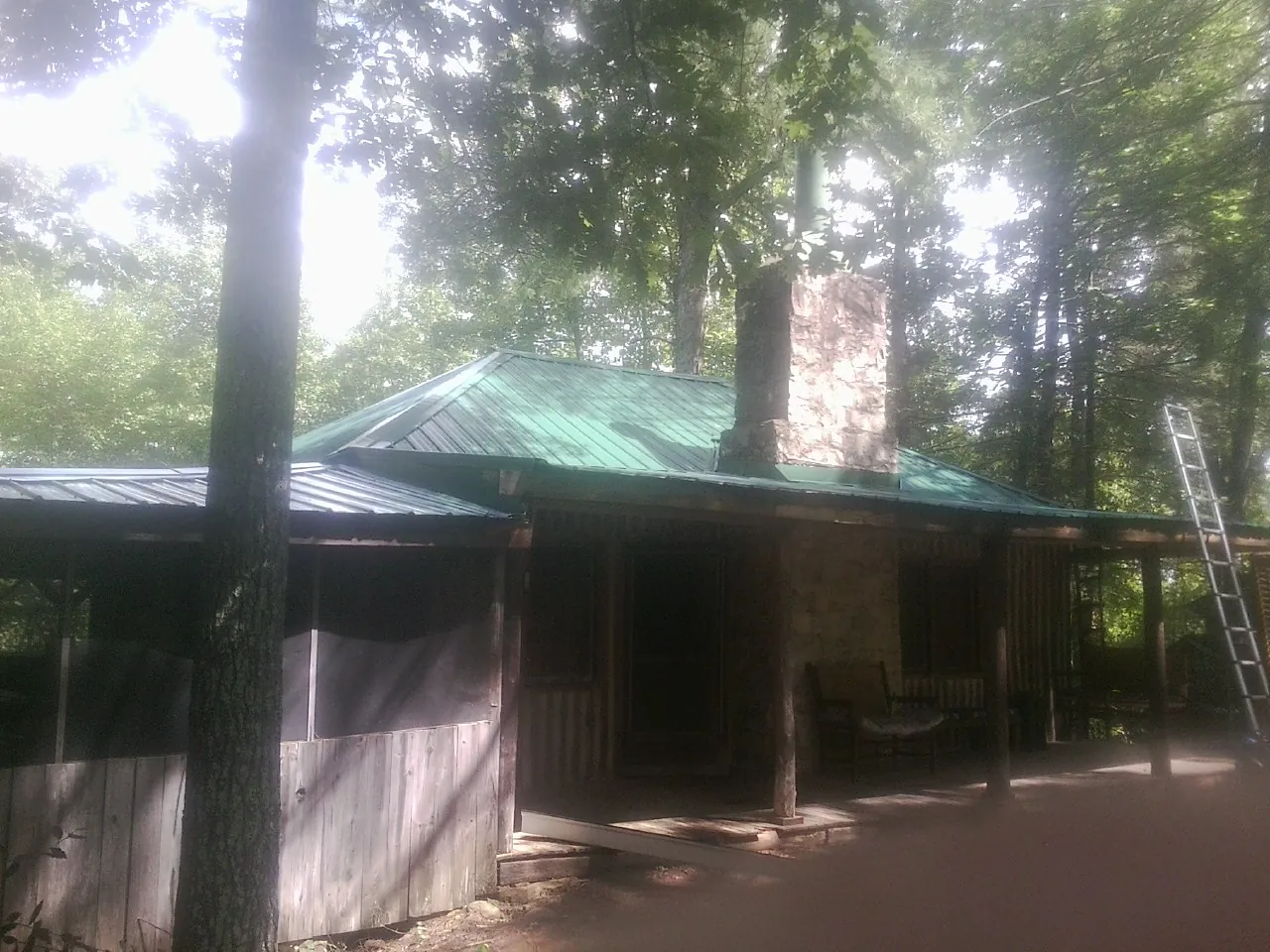 Green metal roof and stone chimney above a log cabin porch in Lyons