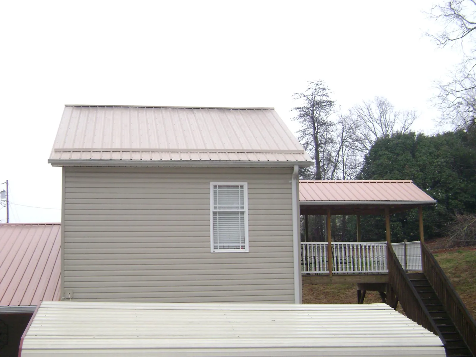 Tan metal roofs on a two story addition and attached porch, from a Roof Replacement job in Lyons